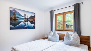 Una camera da letto con un letto, una finestra con tende, un dipinto che raffigura un paesaggio montano e una testata del letto in legno.