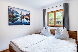 Ein Schlafzimmer mit Bett, einem Fenster mit Vorhängen, einem Gemälde einer Berglandschaft und einem hölzernen Kopfteil.