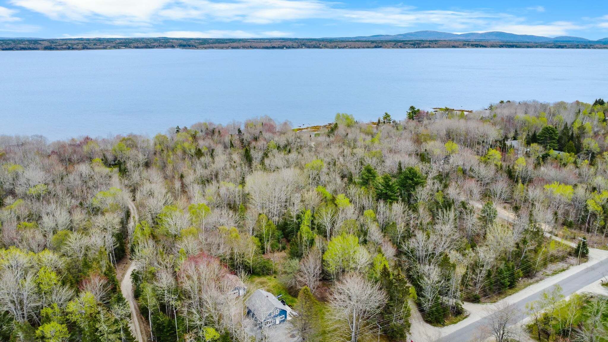Ein Haus, umgeben von einem Wald, mit einem See und Bergen im Hintergrund.