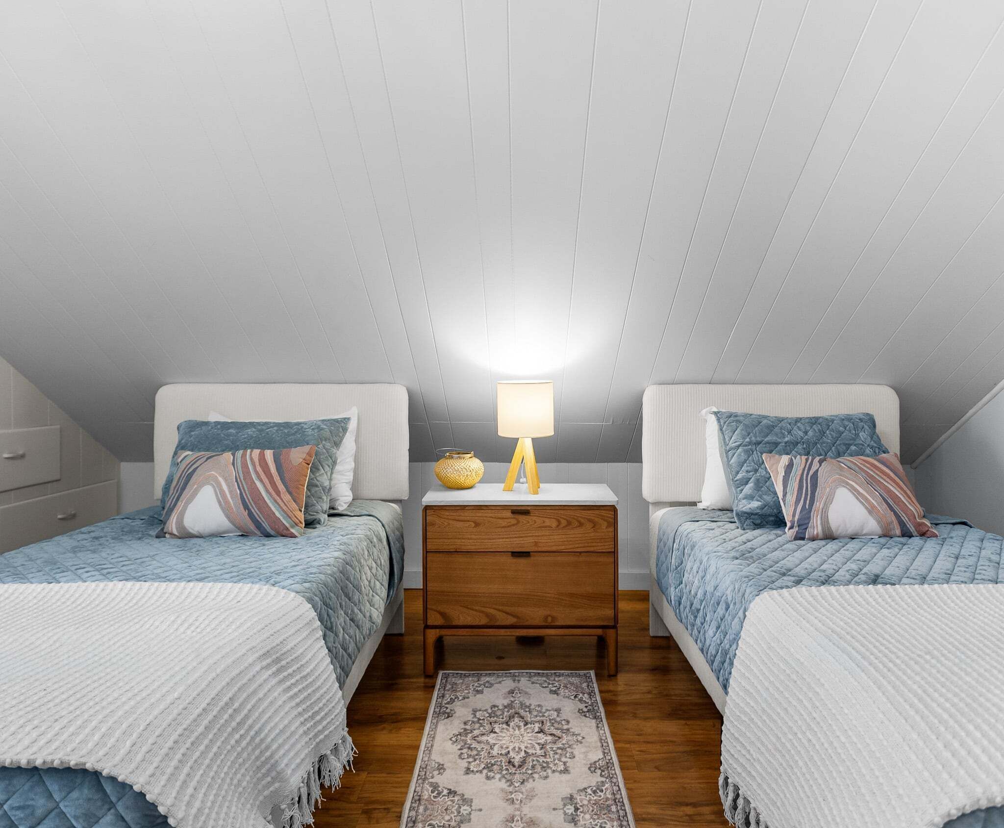 Een slaapkamer met twee bedden, een nachtkastje, een lamp en een vloerkleed.