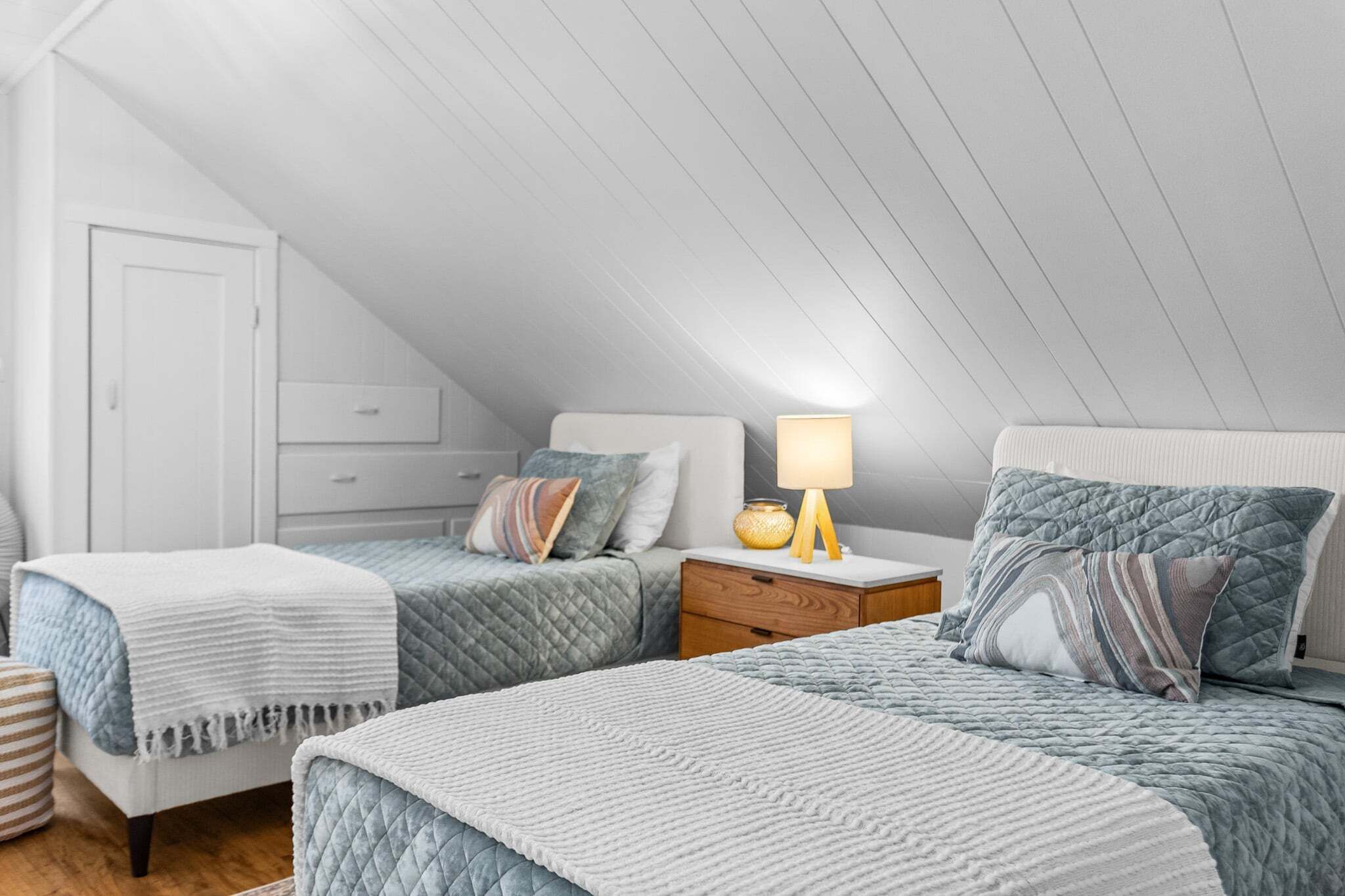 Ein Schlafzimmer mit zwei Betten, einem Nachttisch, einer Lampe und einer Tür.
