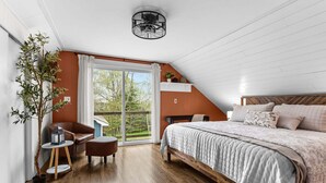 Een slaapkamer met een bed, een stoel, een klein tafeltje, een bloempot en een raam met uitzicht op bomen.