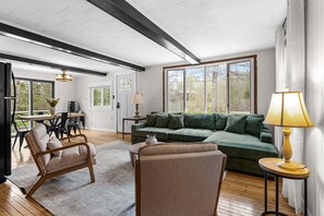 Ein großzügiger Wohnbereich mit einem grünen Sofa, Holzstühlen, einem Esstisch und großen Fenstern.