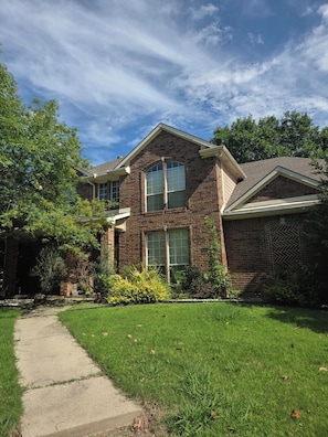 A two-story brick house with a front yard, a pathway leading to the entrance, and a large window on the second floor.