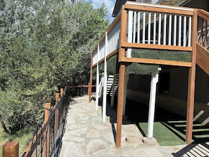 A wooden deck with a railing, a stone pathway, and a view of a building with a staircase.