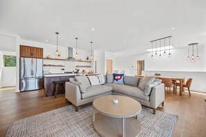 Eine moderne Küche mit integriertem Backofen, ein Essbereich mit Holztisch und -stühlen sowie ein Wohnzimmer mit großzügigem Ecksofa und Couchtisch.
