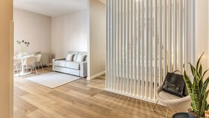 A modern living room with a white sofa, a dining area with a white table and chairs, and a potted plant. - Casa Vostra Vaticano (Rome)