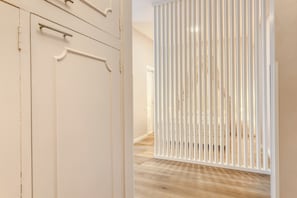 Un pasillo con piso de madera, puertas blancas y un separador blanco con listones verticales.