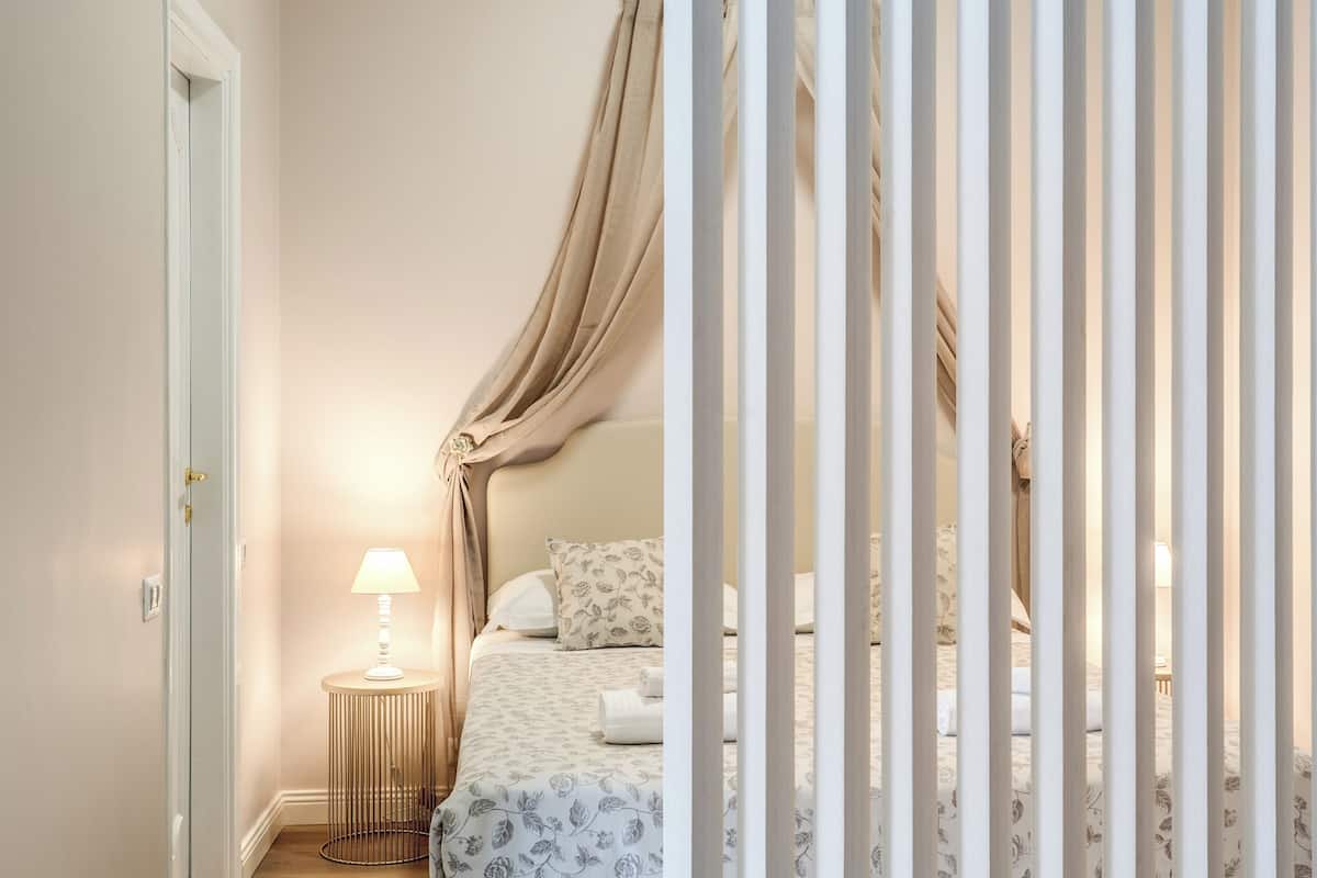 Un dormitorio con cama, mesita de noche y lámpara, y una cortina.