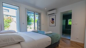 A bedroom with a bed, two windows, an air conditioning unit, and a door leading to a bathroom. - Villa 5 ch. Mer et Rivière entre Nice & Cannes (Villeneuve-Loubet)