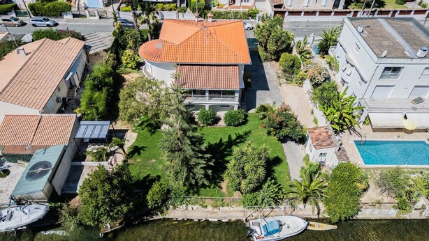 An aerial view of a residential area with a house featuring a red-tiled roof, a swimming pool, and a boat docked by the water. - Villa 5 ch. Mer et Rivière entre Nice & Cannes (Villeneuve-Loubet)