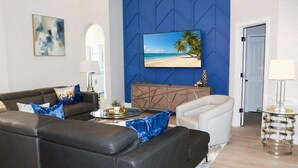 A living room with a sofa, armchair, and a TV mounted on a blue wall. - Stunning Pool Home With Golf Course Views (Davenport)