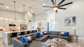 A modern kitchen with a central island, a dining area with a glass coffee table, and a living room with a sectional sofa. - Stunning Pool Home With Golf Course Views (Davenport)