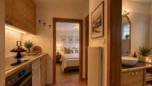 Una cocina moderna con horno empotrado, un comedor con mesa y sillas redondas, y un dormitorio con cama y mesitas de noche.