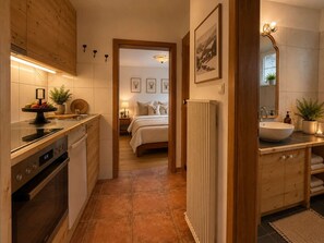 Eine moderne Küche mit Einbauofen, eine Essecke mit rundem Tisch und Stühlen sowie ein Schlafzimmer mit Bett und Nachttischen.