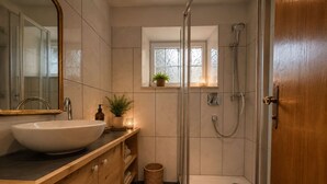 Un baño moderno con un lavamanos grande, tocador de madera, cabina de ducha de vidrio y una pequeña ventana con una planta.