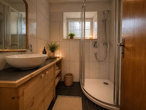 Ein modernes Badezimmer mit einem großen Waschbecken, einem Holzkosmetikschrank, einer Glasdusche und einem kleinen Fenster mit einer Pflanze.