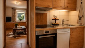 Una cocina con armarios de madera, horno empotrado, lavavajillas y una ventana con cortinas.