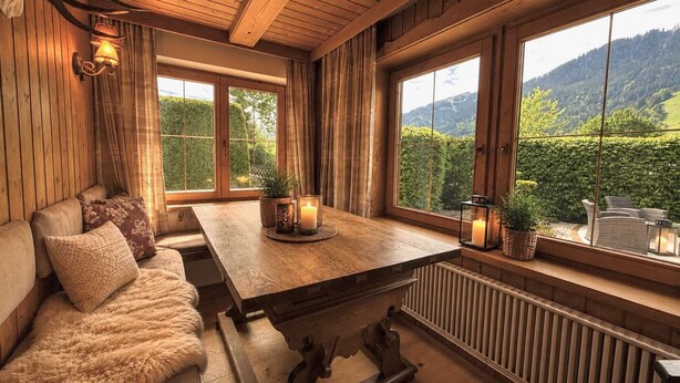 Una habitación acogedora con una mesa de madera, sofá y ventanas amplias que ofrecen vista a un paisaje verde.