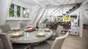 A dining area with a glass table, wicker chairs, and a staircase. - Cottonwood Port Douglas (Oak Beach)
