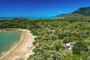 Luftaufnahme einer Küstenimmobilie mit Strand, dichtem Wald und einem Haus mit Pool.