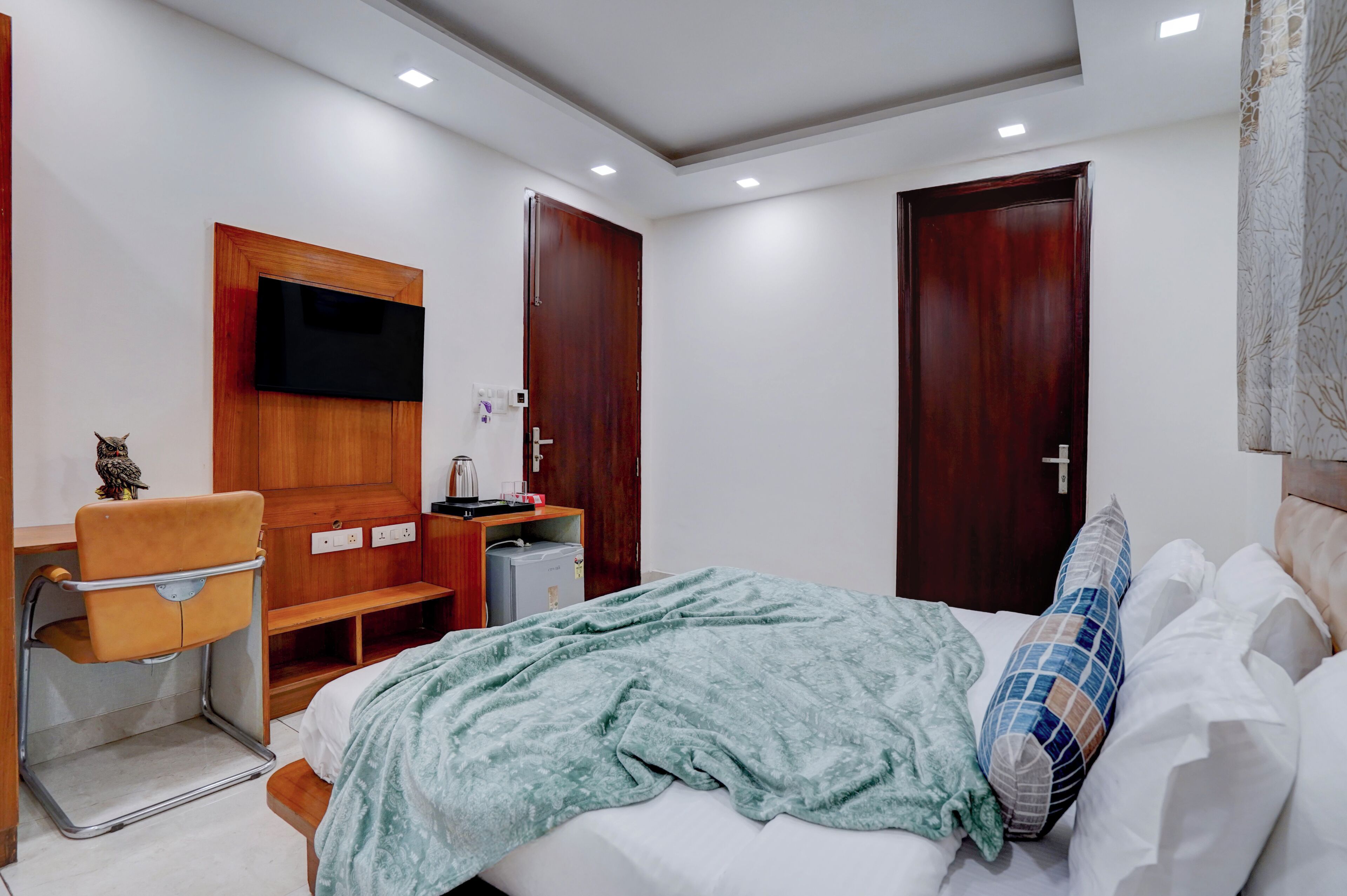 A modern hotel room with a bed, a desk with a chair, a television mounted on the wall, and a wardrobe.