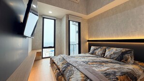 Un dormitorio moderno con una cama grande, un televisor montado y vistas a la ciudad desde la ventana.