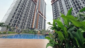 Un edificio residencial alto con varios balcones, piscina y vegetación circundante.