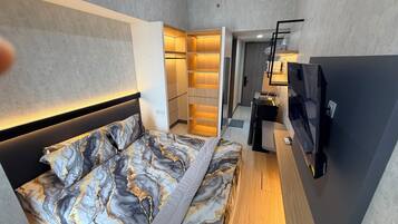 A modern hotel room with a bed, a desk, a TV, and a walk-in closet.
