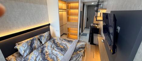 A modern hotel room with a bed, a desk, a TV, and a walk-in closet.