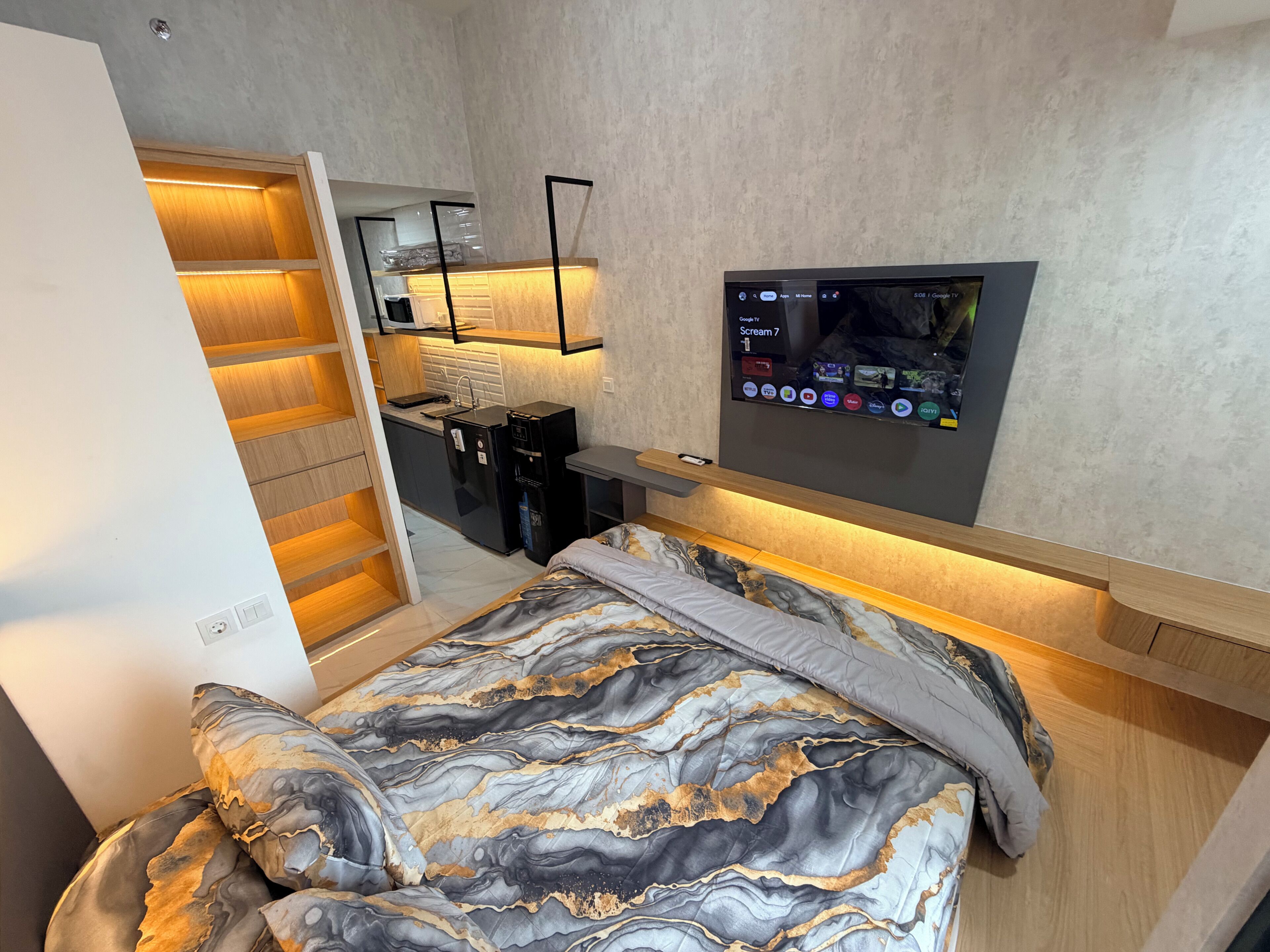 Une chambre compacte comprenant un lit, un téléviseur encastré, une petite kitchenette et un dressing.