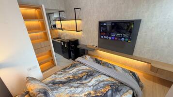 Une chambre compacte comprenant un lit, un téléviseur encastré, une petite kitchenette et un dressing.