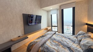 Un dormitorio moderno con cama, televisor montado, ventana con vista a la ciudad y balcón.