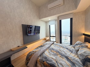Quarto moderno com cama, televisão na parede, janela com vista para a cidade e varanda.