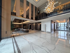 Um hall amplo com teto alto, piso de mármore e luminárias modernas.