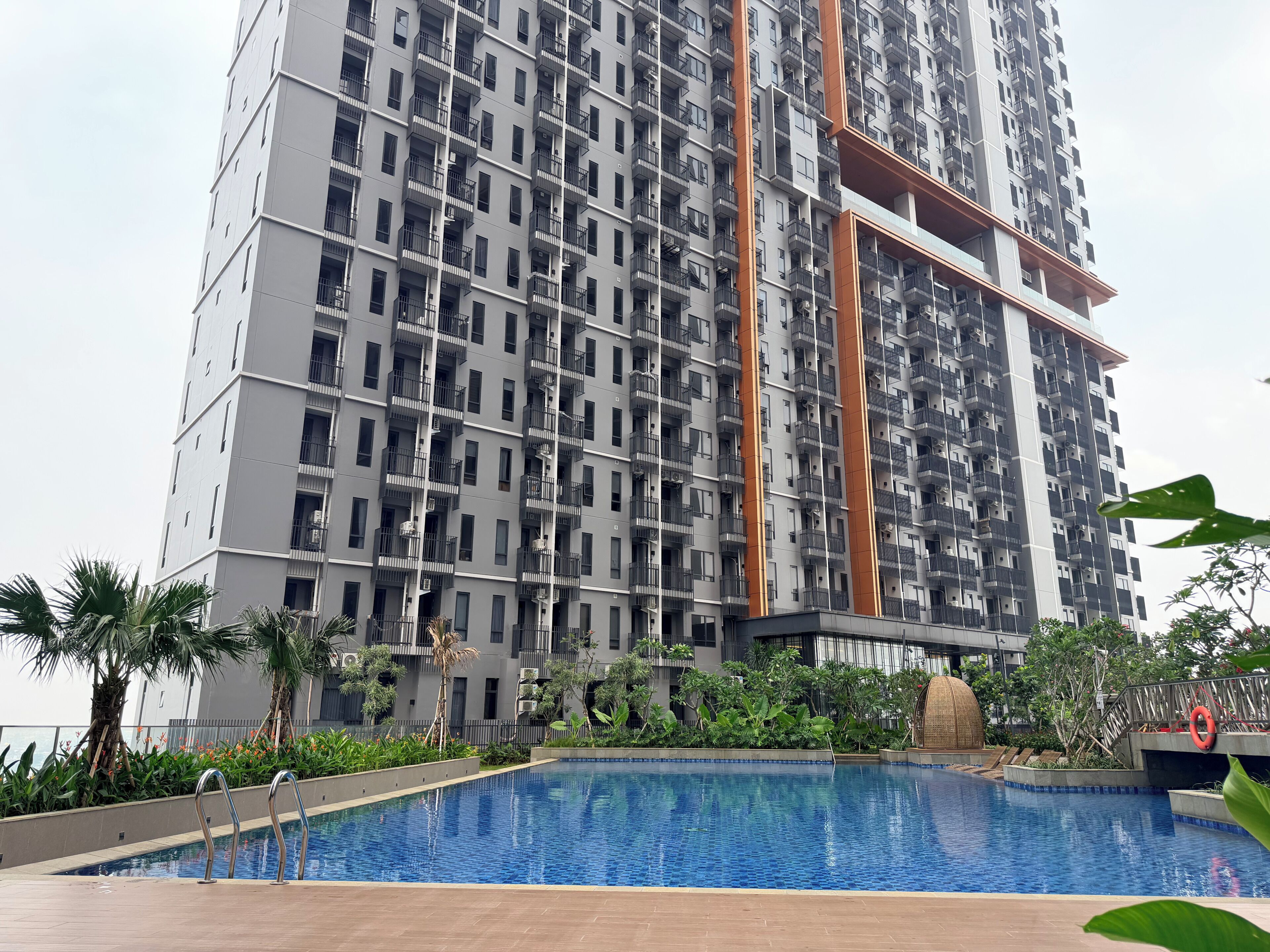 A high-rise residential building with multiple balconies, a swimming pool, and surrounding greenery.