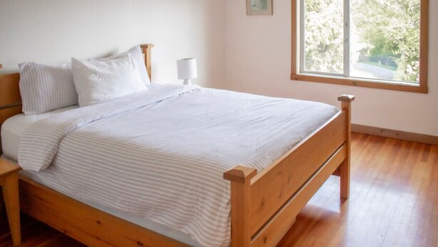 A wooden bed in a room with a window, a bedside table, and a wall-mounted picture. - Tower House  - West Coast Forest Escape (Ucluelet)