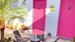 Un patio con una mesa redonda y seis sillas, dos puertas rosadas y una palmera.