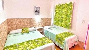 Una habitación con dos camas, una lámpara de pared, un cuadro enmarcado y un ventanal con cortina.