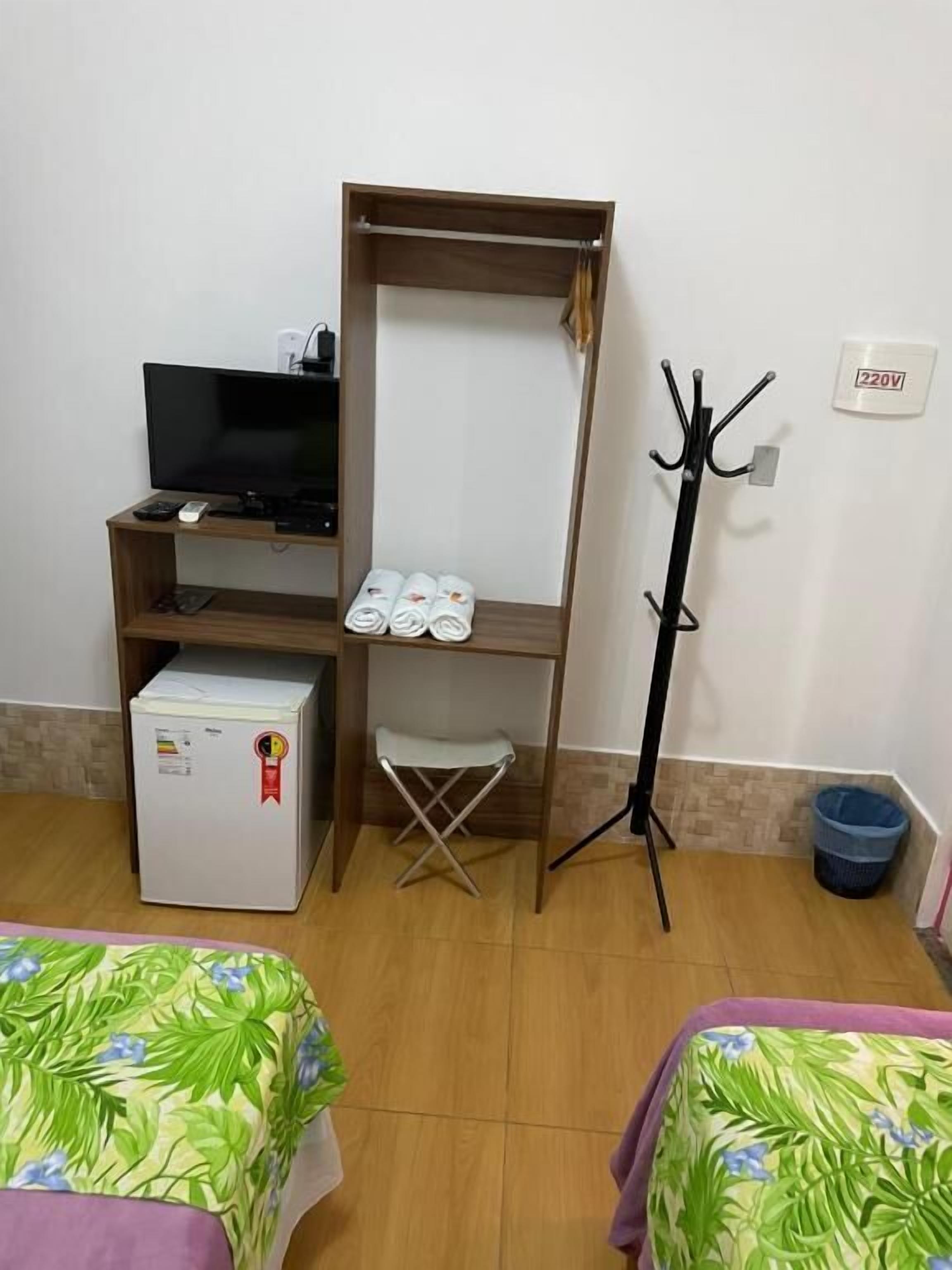 A room with a TV, a mini-fridge, a coat rack, and a small stool.