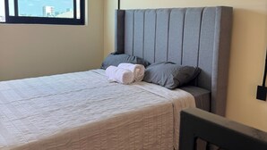 A neatly made bed with a grey headboard, a window with a city view, and a power outlet on the wall. - Beautiful loft in Chapultepec (Guadalajara)