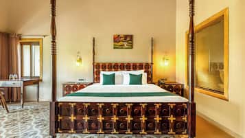 Una cama con dosel de madera y colcha verde, un escritorio con silla, y un cuadro en la pared.