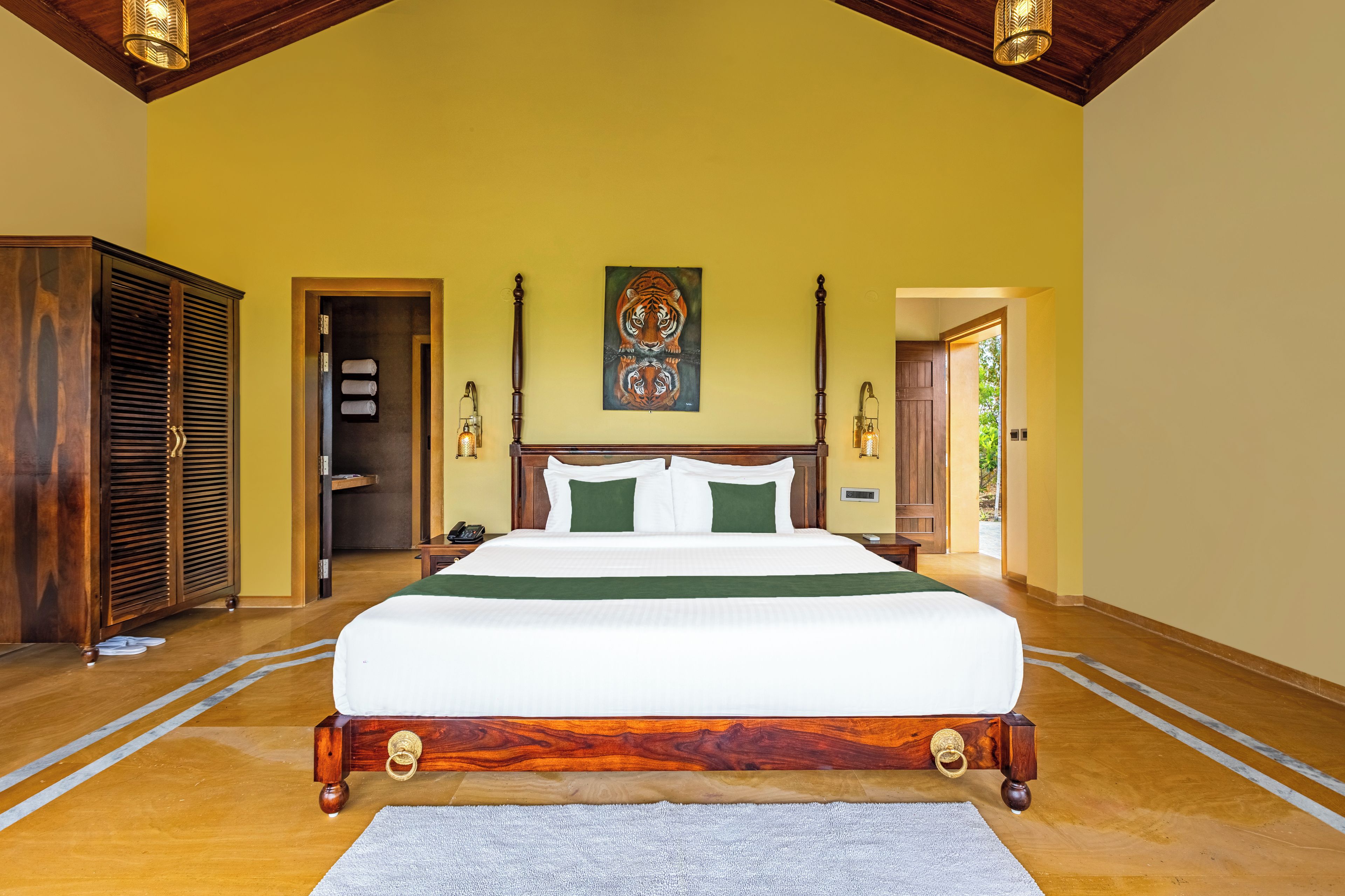 Una cama grande con estructura de madera y ropa de cama verde, un cuadro de un tigre en la pared y un armario de madera.