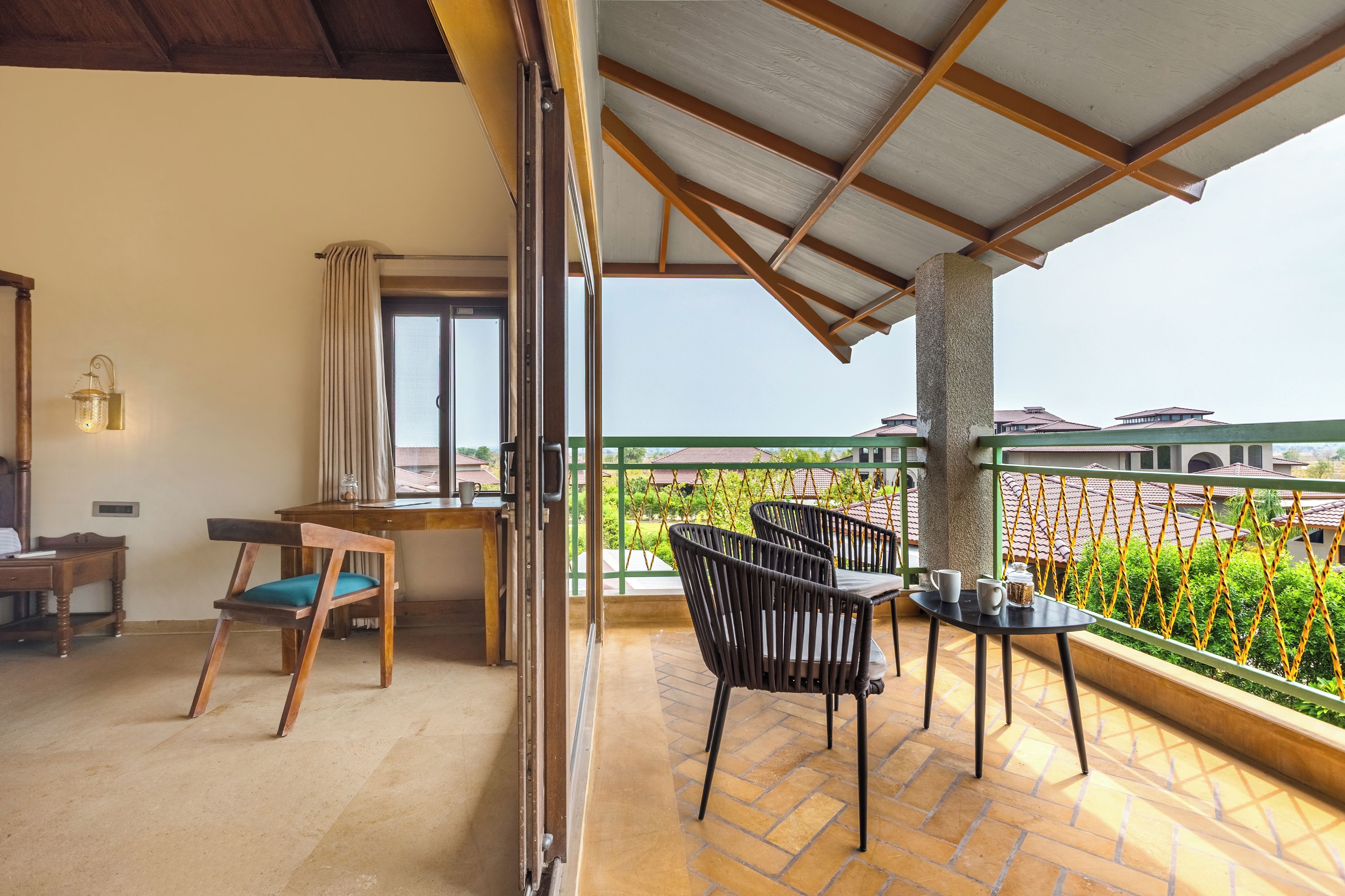 Un balcón con vista a una zona residencial, un escritorio de madera, una silla y una mesa con dos sillas.