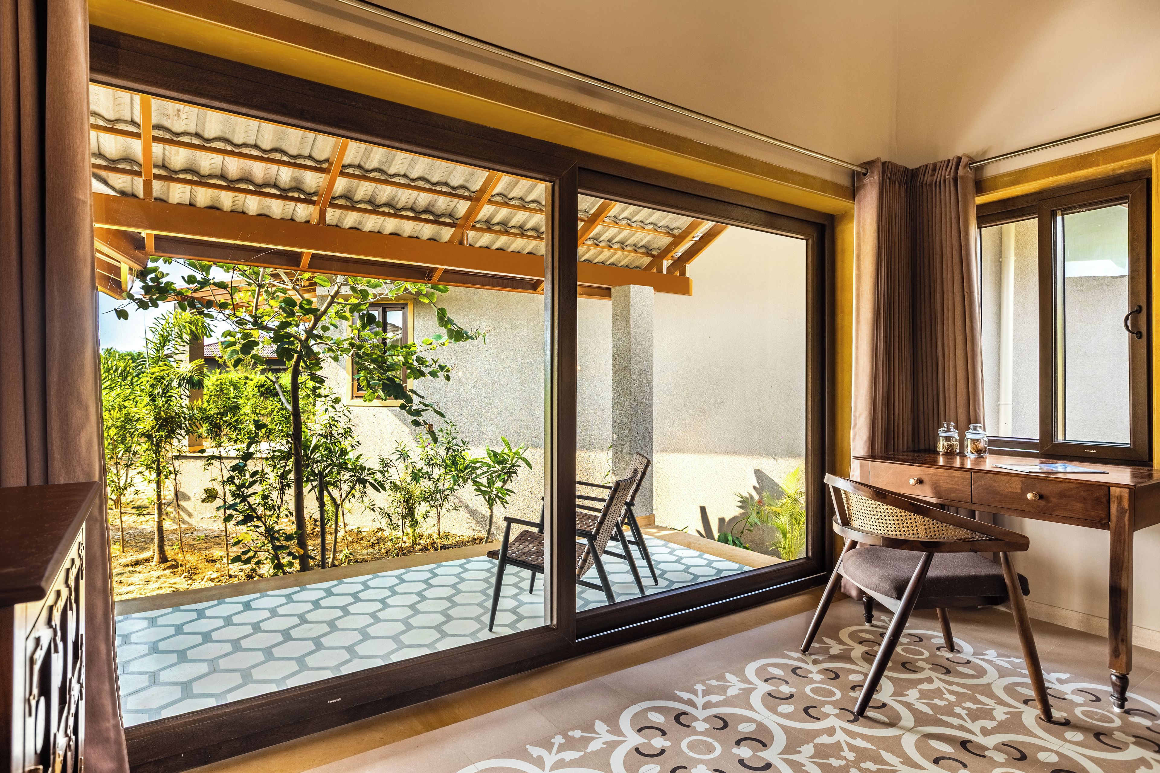 Una habitación con un gran ventanal corredero que da a un espacio exterior con plantas y suelo de baldosas.