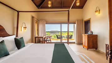 Habitación de hotel con una cama grande, cabecera de madera, balcón con vistas y cómoda de madera.
