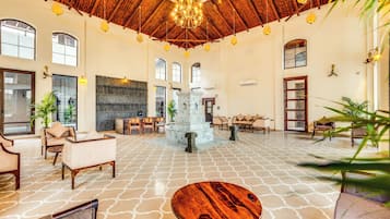 A spacious lobby with a high ceiling, chandeliers, and a central fountain.