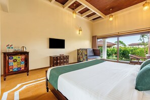 A bedroom with a large bed, a television mounted on the wall, a wooden cabinet with a colorful quilt, and a view of the outdoors through a large window.
