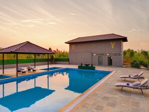A swimming pool with lounge chairs and a gazebo, surrounded by a landscaped garden and a building with a tiled roof.