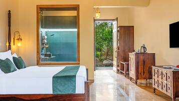 Habitación de hotel con cama, baño con puerta de vidrio, armario de madera y televisor en la pared.